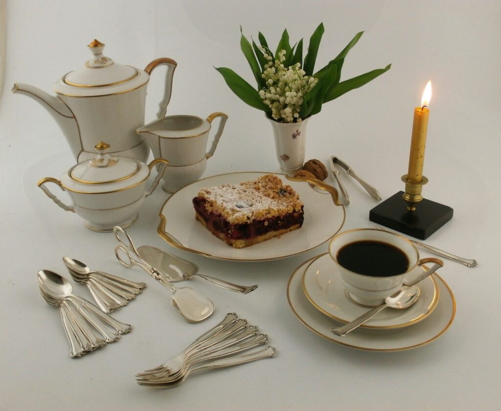 stara porcelana, kawa w filiżance, ciasto na talerzyku, świecznik z zapaloną świecą.